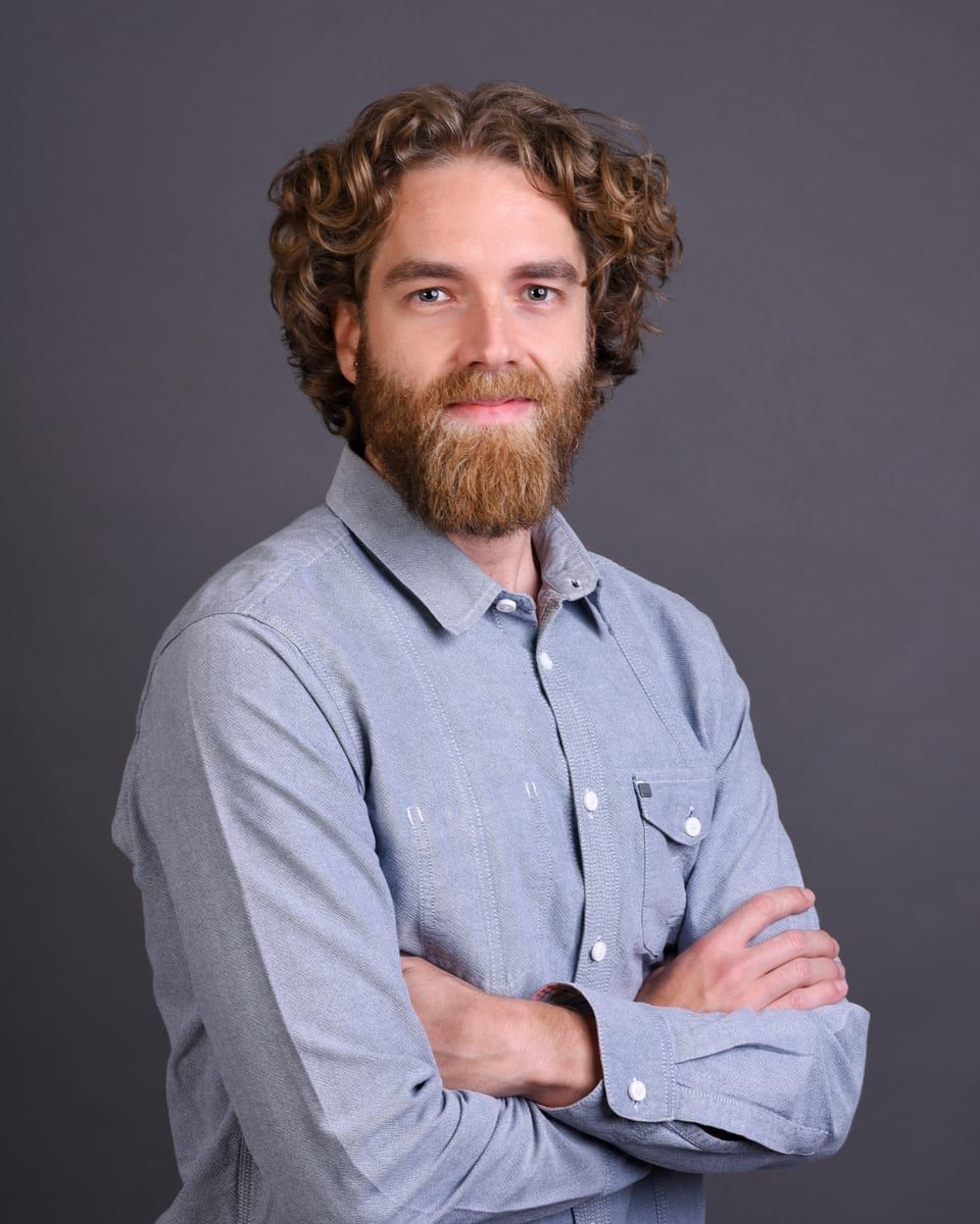 Christian Rüst, smiling, arms crossed, in a light-blue shirt against a grey backdrop