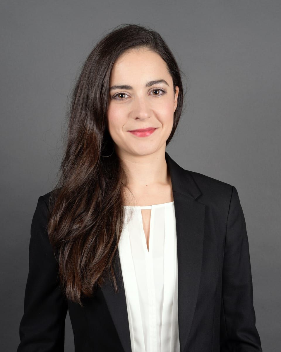 Corina Rüst, smiling, in a black blazer and white blouse against a grey backdrop
